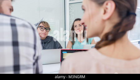 Vue latérale d'une femme créative freelancer souriant à son collègue, tout en faisant un appel sur le téléphone mobile à un bureau partagé dans une ambiance de l'environnement de travail Banque D'Images