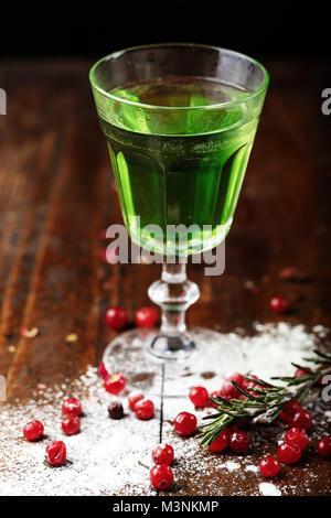 Vert Absinthe forte boisson alcoolisée dans un verre sur le bar, à côté de petits fruits dispersés de canneberges Banque D'Images