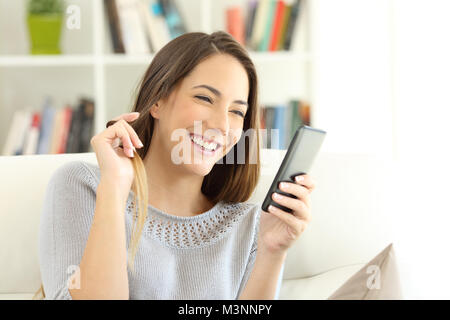 Fille de flirter en ligne avec un téléphone intelligent assis sur un canapé dans la salle de séjour à la maison Banque D'Images