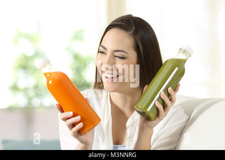 Happy woman on compare deux légumes, assis sur un canapé dans la salle de séjour à la maison Banque D'Images