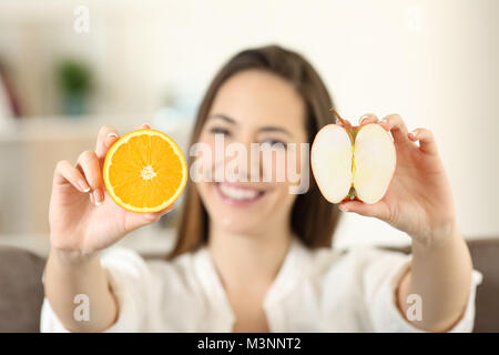 Vue avant portrait d'une femme heureuse montrant une orange et apple assis sur un canapé dans la salle de séjour à la maison Banque D'Images