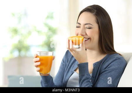 Happy woman smelling une orange et le jus d'un assis sur un canapé dans la salle de séjour à la maison Banque D'Images