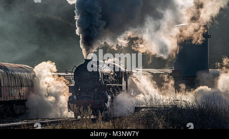 La locomotive du train à vapeur à l'approche d'un passage dans une gare de triage des marchandises en laissant de la fumée et de la vapeur à partir de derrière la création de la photographie Banque D'Images