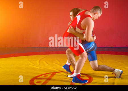 Deux lutteurs forte en bleu et rouge wrestling collants sont wrestlng et faisant la pince sur un tapis de lutte jaune dans la salle de sport. Banque D'Images