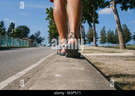 Un homme marche le long du bord de la route dans un pays tropical chaud. Banque D'Images