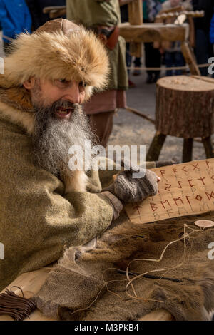 York, UK, le 12 février 2018. Un homme barbu habillé en Viking Jorvik Viking à l'assemblée annuelle du Festival. Assis à l'extérieur, il explique l'alphabet runique, en pointant sur les runes gravés sur une planche de bois. Il prend part à une reconstitution réaliste de la vie à un marché Viking. Centre ville de York, North Yorkshire, England, UK. Crédit : Ian Lamond/Alamy Live News Banque D'Images