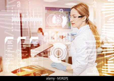 Jeune médecin habile assis au microscope et à occupé Banque D'Images