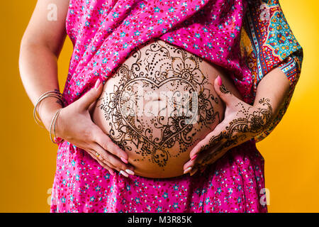 Une photo couleur d'un tatouage au henné sur le ventre d'une femme enceinte, sur fond jaune. Banque D'Images