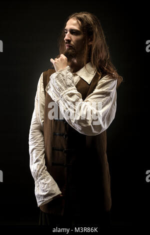 Photo de barbu en costume pirate sur fond noir, tire sur sa barbe pirate pensif Banque D'Images