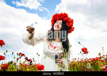 Heureux, jeune femme enceinte porte couronne au champ de coquelicots à jouer avec des bulles de savon Banque D'Images