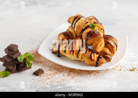 Des croissants frais avec du sirop de chocolat sur un fond gris clair, copiez l'espace. La cuisine française dessert concept. Banque D'Images