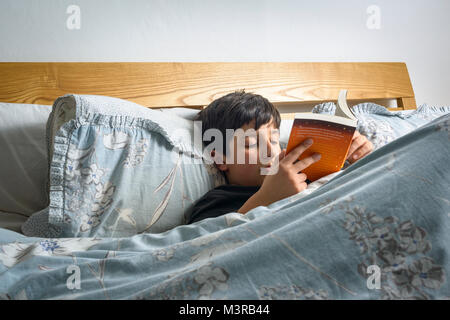 Boy reading a book in bed ,,UK Banque D'Images