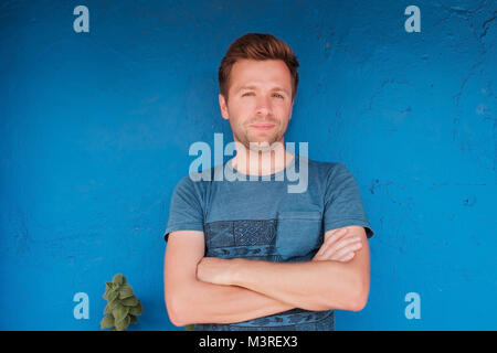 Portrait of smiling young caucasian man standing près de mur bleu avec freen leaf Banque D'Images