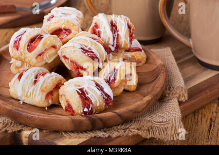 Pile de pâtisseries aux fraises sur une plaque de bois avec des tasses à café en arrière-plan Banque D'Images