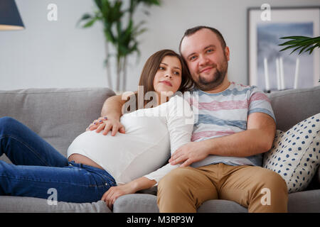 Photo de l'avenir heureux parents assis sur le canapé gris Banque D'Images