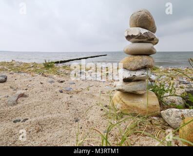 Pierre pyramide équilibrée sur le rivage de l'eau bleue de la mer. Blue cloudy sky du niveau de l'eau miroir. De mauvaises conditions de luminosité. Banque D'Images