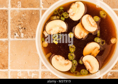 Bol de soupe claire de style japonais avec des champignons et oignons de printemps sur une table de cuisine carrelée Banque D'Images