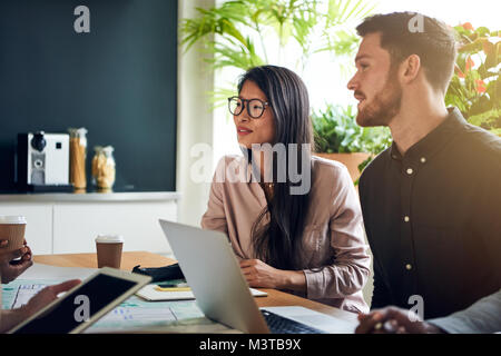 Deux collègues divers smiling assis ensemble à une table de conférence dans un bureau d'une réunion avec les collègues Banque D'Images