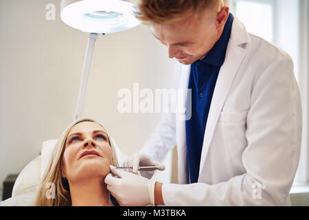 Jeune homme médecin d'effectuer des injections de botox pour le menton d'un couple sur une table dans une clinique de beauté Banque D'Images