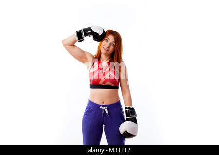 Jeune femme rousse dans les vêtements de sport et des gants de boxe noir et blanc sourit et se frappe sur la tête fort sur blanc fond isolé... Banque D'Images