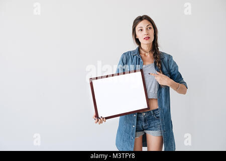 Jeune fille hipster montrant avec le doigt sur papier blanc dans l'image ou l'étiquette demandée, brochure, maquette, carte vierge, de l'affiche. Habillé en fille occasionnels den Banque D'Images