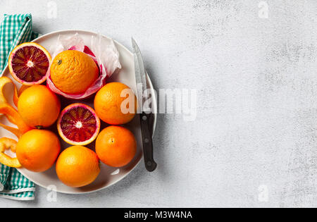 Un groupe d'oranges sur une assiette. Certains d'entre eux réduit. couteau et serviette. sur un fond en pierre. une table d'été en bonne santé, la préparation de jus d j Banque D'Images