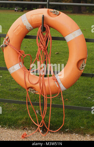 Une bouée orange suspendu par une clôture métallique par un sentier attaché à longue longueur d'orange, la corde de nylon avec de l'herbe en arrière-plan Banque D'Images