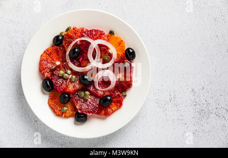 De style espagnol typique salade d'orange, l'oignon rouge et les olives avec les câpres et les matières premières fraîches Huile d'olive et du jus de citron vert . Servi sur un tableau blanc en pierre de l'été. Banque D'Images