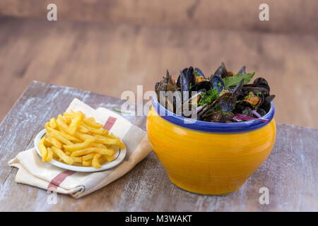 Moule bleue française avec des herbes dans un bol jaune avec frites ramequin verre serviette sur des fruits de mer dans une planche en bois historique Banque D'Images