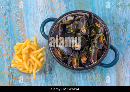 Moules dans un pot en céramique bleu sur un fond de bois bleu. avec un bol en verre de frites. Mode de vie méditerranéen. Banque D'Images