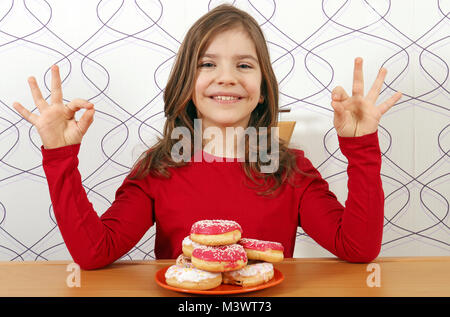 Happy little girl avec des beignets sucrés et signes des mains ok Banque D'Images