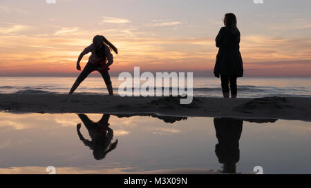 Incroyable coucher de soleil avec des reflets sur la mer guestig encore deux silhouettes se reflétant dans l'eau de mer sur la plage Banque D'Images