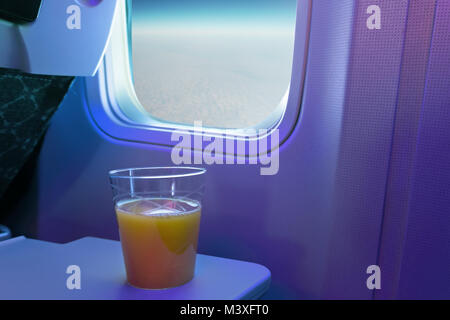 Une tasse de jus d'orange sur le bac à son siège ou d'un aéronef. Verre de verre sur l'arrière-plan de la fenêtre de l'avion. Voler au-dessus des nuages. Banque D'Images