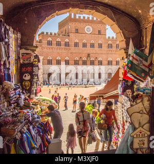 Mère et enfant marchent à travers une entrée à la place médiévale 'il Campo' de Sienne avec le Palazzo Pubblico en arrière-plan. Banque D'Images