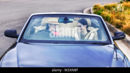 Les jeunes femmes au volant d'une voiture décapotable de luxe moderne avec capote ouverte sur une journée ensoleillée pleine de joie et de bonheur - vue à travers le pare-brise. Banque D'Images