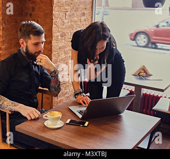 Un homme avec des bras tatoués et femelle brune à l'aide d'un ordinateur portable dans un Banque D'Images