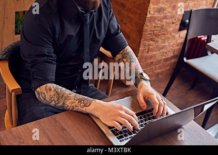 Un homme avec des bras tatoués de travailler avec un ordinateur portable. Banque D'Images