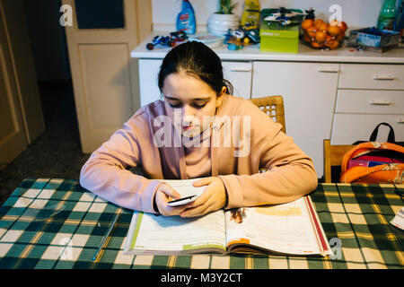 Adolescent fait ses devoirs dans la cuisine sur la table elle-même aider avec le smartphone Banque D'Images