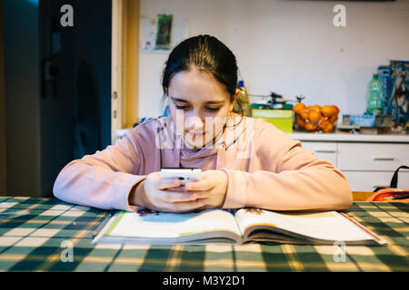 Adolescent fait ses devoirs dans la cuisine sur la table elle-même aider avec le smartphone Banque D'Images