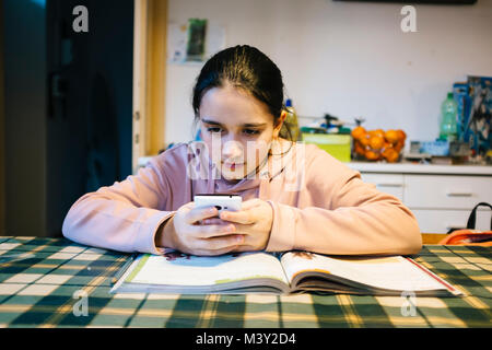 Adolescent fait ses devoirs dans la cuisine sur la table elle-même aider avec le smartphone Banque D'Images