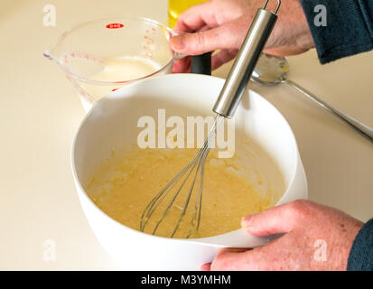 Man pouring milk à la pâte pour faire une pâte à crêpes pour Mardi Gras avec la farine, le lait, les œufs et l'huile dans une cuisine maison Banque D'Images