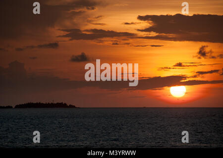 Fiery lumineux coucher du soleil sur l'océan : un ballon rond de soleil se couche à l'eau au milieu des nuages gris, à gauche est le contour noir de l'île. Banque D'Images