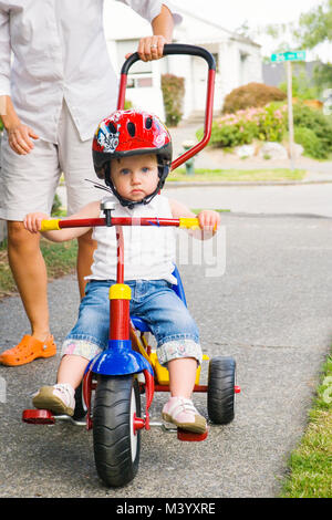 Une mère poussant un bébé fille sur son tricycle sur un trottoir du quartier. Banque D'Images