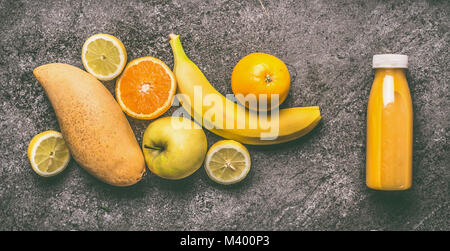 Smoothie aux fruits jaune avec du citron, orange, pomme, banane et mangue en bouteille sur table en granit gris , vue d'en haut. Suivre un régime sain et antioxidan Banque D'Images