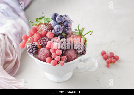 Assortiment de petits fruits surgelés en blanc tasse sur la pierre de fond béton Banque D'Images