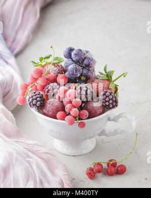 Assortiment de petits fruits surgelés en blanc tasse sur la pierre de fond béton Banque D'Images