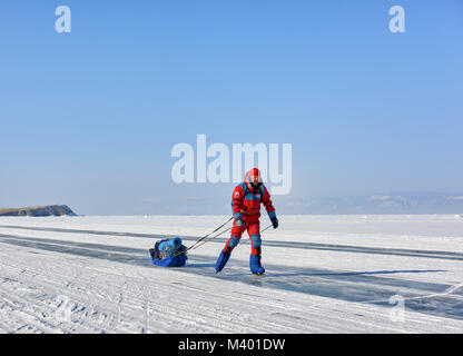 Le lac Baïkal, région d'Irkoutsk, RUSSIE - 08 mars 2017 : l'homme à une orange salopette polaire est le patinage. Vacances actives en hiver en Sibérie Banque D'Images