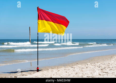 Panneau d'avertissement jaune et rouge d'un drapeau marquant la limite de la zone de baignade en toute sécurité sur une plage sous un ciel d'été bleu Banque D'Images