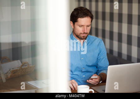 Jeune homme la lecture de messages texte en ligne tout en travaillant de chez vous. Banque D'Images