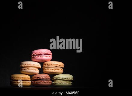 Macarons de bon goût différent dans une tache de lumière sur un fond sombre Banque D'Images